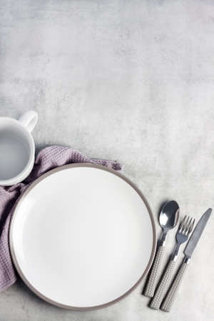 Table setting. White plate, mug, cutlery and napkin on light gray background. Flat lay, top view, copy space.の写真素材