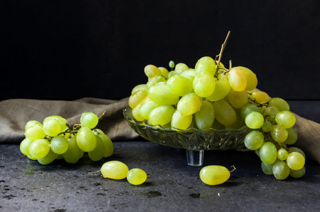 Fresh ripe green grapes in a glass fruit bowl on black background