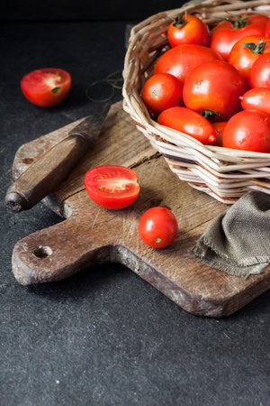 Fresh red tomatoes in whicker basket on black background. Copy space