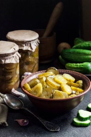 Pickled cucumber salad in a bowl and jars on black backgroundの写真素材