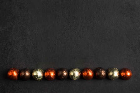 Line of chocolate candies wrapped in multicolored foil on black background with copy space. Top view, flat layの写真素材