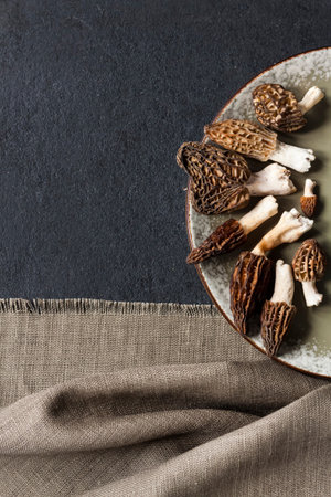 Morel mushrooms on a plate on black background. Flatlay, copy space
