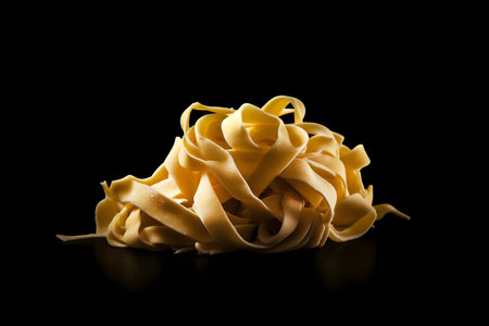 Uncooked tagliatelle pasta isolated on black background. Generative AI contentの素材