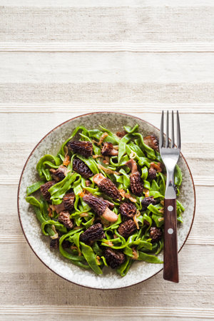 Homemade green nettle pasta with fried spring morel mushrooms on a plate. Flat lay, top view, copy spaceの写真素材