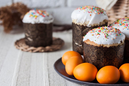 Glaze decorated Easter cakes and orange colored eggs on a plate closeup.