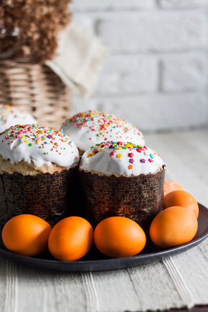 Closeup of glaze decorated Easter cakes and yellow colored eggs on a plate on the table.