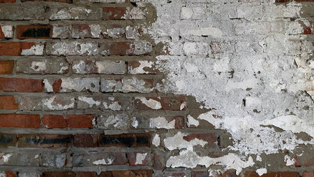A close-up of a weathered brick wall with peeling white paint, showcasing the rough texture and aged appearance of the surface.の写真素材