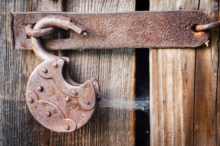 Old opened rusty padlock and spider web on wooden backgroundの写真素材