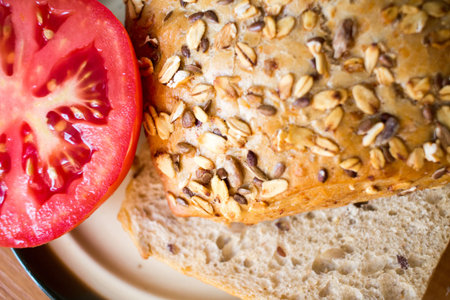 Composition of whole grain bread buns and red fresh cut in half tomato on a plate on wooden table...