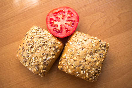 Composition of whole grain bread buns and red fresh cut in half tomato on wooden table backgroundの写真素材