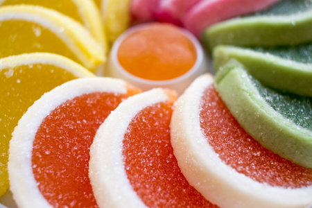 Close up of round Composition of colorful jellies (green, orange, yellow, purple) in a shape of a half moon in a white box with one round jelly in the middle on wooden background. Rainbow of colorsの写真素材
