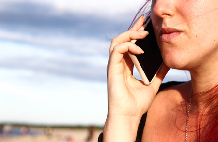 Detail of young girl speaking via mobile telephone on the beach at seaの写真素材