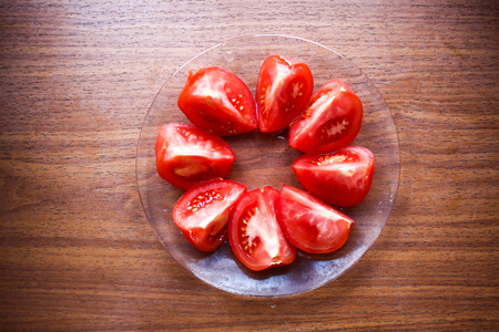 Round circle of cut tomatoes close up on a glass plate on wooden table backgroundの写真素材