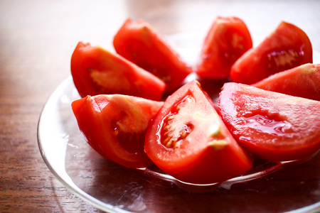 Round circle of cut tomatoes close up on a glass plate on wooden table backgroundの写真素材