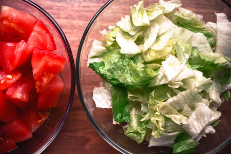 Cut tomatoes and lettuce for preparing food in glass bowls on wooden backgroundの写真素材