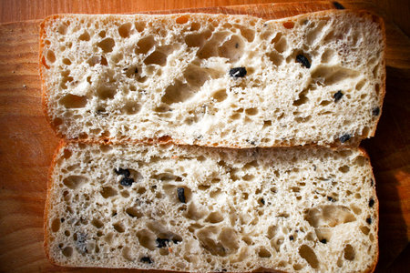 Cut Bread bunn with olives on wooden board on wooden background close up focus