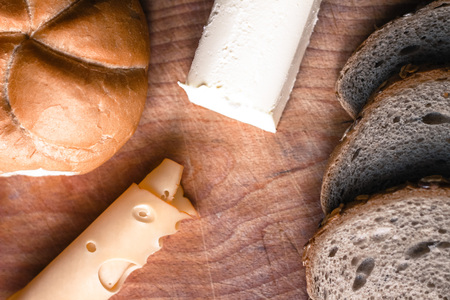Freshly baked brown bread bunn, slice of smoked yellow cheese and piece of butter on wooden background. Healthy and tasty traditional breakfast or snackの写真素材