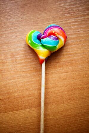 Colorful rainbow red purple yellow blue green colors: lolipop in a shape of heart on a stick on wooden backgroundの写真素材