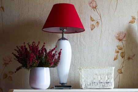 Red lamp and white vase with flowers in a room with soft light on a white wallpaper with flowersの写真素材