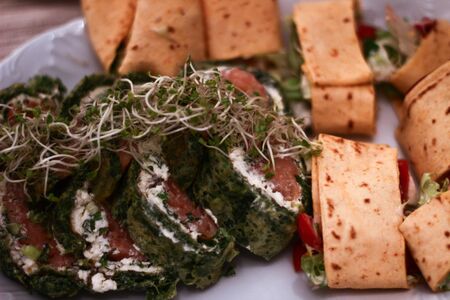 Cut tortilla slices with vegetables and spinach pie with salmon slices and shoots. Party food in Polandの写真素材
