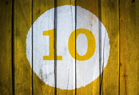 House number or calendar date in white circle on yellow toned wooden door background. Number ten 10の写真素材