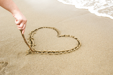 Nice, pleasant and simple sunny summer composition on holidays. Happy relaxing vacations. Hand drawn with stick on sand on beach with stick: heart with wavesの写真素材