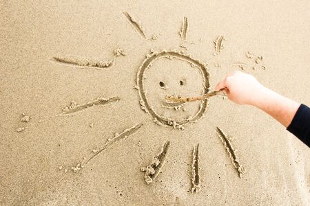 Nice, pleasant and simple sunny summer composition on holidays. Happy relaxing vacations. Hand drawn with stick on sand on beach with stick: smiling sunの写真素材