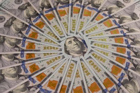 A close-up of many hundred-dollar bills lie in an even circle.