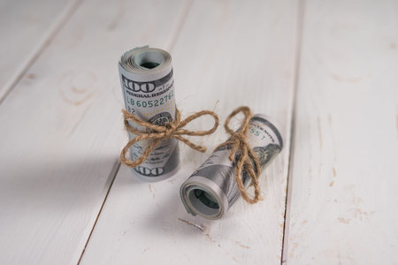Two stacks of hundred-dollar bills tied with a rope on a light background.