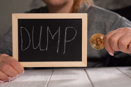 A woman holding a board with the inscription DUMP and a golden bitcoin.の写真素材