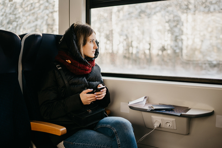 Girl at the black jacket with the cellphone going by the train and watching at the window
