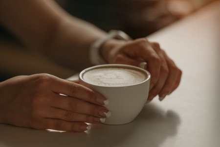 A girl with beautiful nails keeps a cup of latte in her hands in a cafe. の写真素材