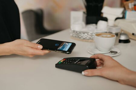 A girl paying for her latte with a smartphone by contactless NFC technology in a cafe. A female barista holds out a terminal for paying to a client in a coffee shop.の写真素材
