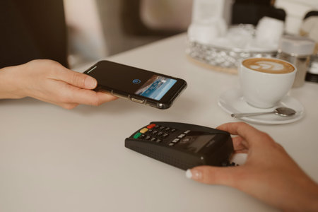 A woman paying for her latte with a smartphone by contactless NFC technology in a cafe. A female barista holds out a terminal for paying to a client in a coffee shop.の写真素材
