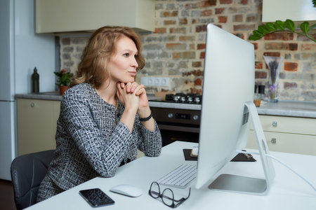 A young woman works remotely on a desktop computer in her studio. A lady sits arms crossed during a...