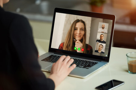 A laptop screen view over a woman's shoulder. A boss listening to a report of an employee on an...