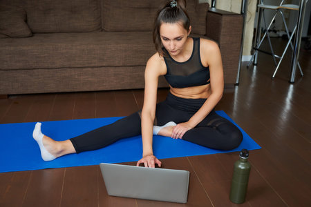 A fitness coach in a tight suit is talking with clients on an online video on a laptop after a...