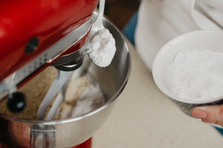 A close photo of the spoonful and a cup of powdered sugar above the stainless steel bowl of the red...
