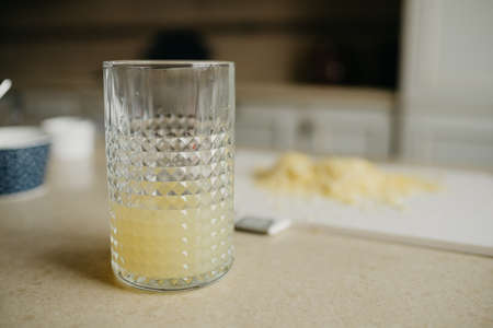 A glass of fresh lemon juice is standing on the table with zest on the background.の写真素材