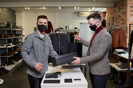 A man in a face mask to avoid the spread of is taking his purchases in a clothing store. A male shop...