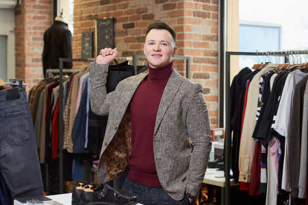 A young man in a sports jacket is posing with his purchases in black paper bags in a clothing store. A happy male customer in a boutique.の写真素材