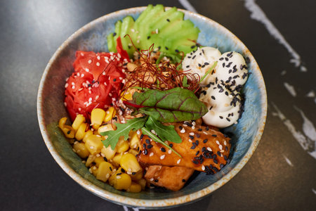 A top view of a poke bowl with tuna, avocado slices, wasabi, corn, peanut, sesame, and Philadelphia...