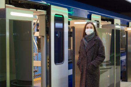 A woman in a medical face mask to avoid the spread of virus is waiting near the modern subway car. A...