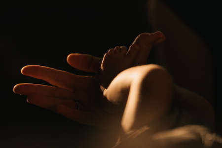 A close-up photo of the gentle hand of the mother who is holding the heels of her newborn baby. The legs of the infant in the sunlight in the evening.の写真素材