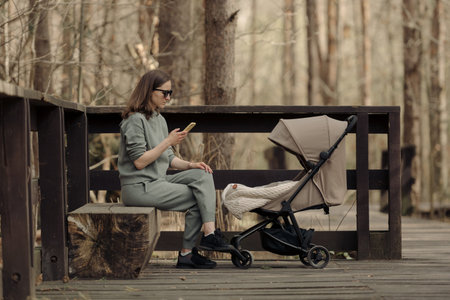 The young mom is working with her cellphone while her infant child is sleeping in the baby stroller....
