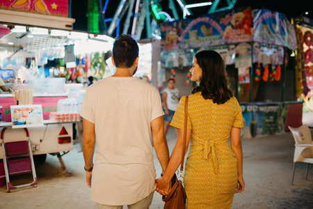 A girl and her boyfriend with their backs are walking between amusement rides.の写真素材