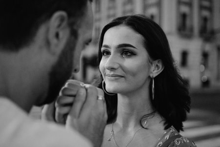 A photo of a girl over a mans shoulder. A guy is kissing the hands of his girl.