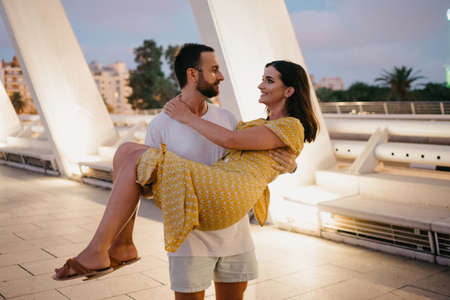 A man with a beard is holding his girl in a yellow dress in his arms in Valenciaの写真素材