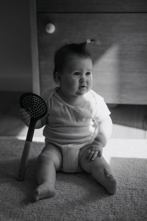 A black and white photo of a 7-month girl is sitting on the carpet
