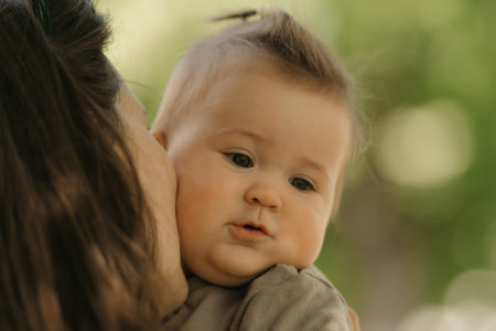 A close portrait of a 7-month girl who is been kissing by her mother in the park